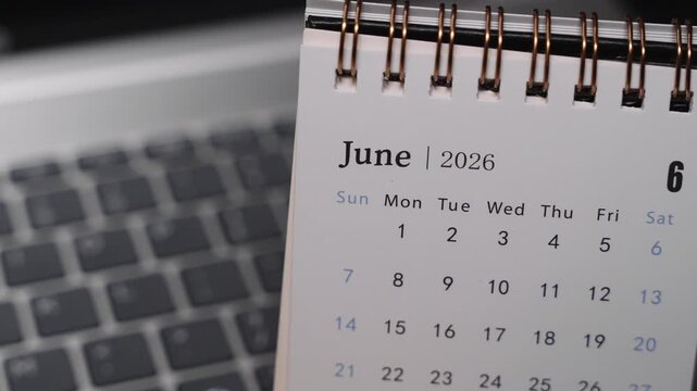 Close-up of a desk calendar on a laptop keyboard as a hand flips the page from May 2026 to June 2026. Camera stays static, showing a clear monthly time transition and structured planning concept indo