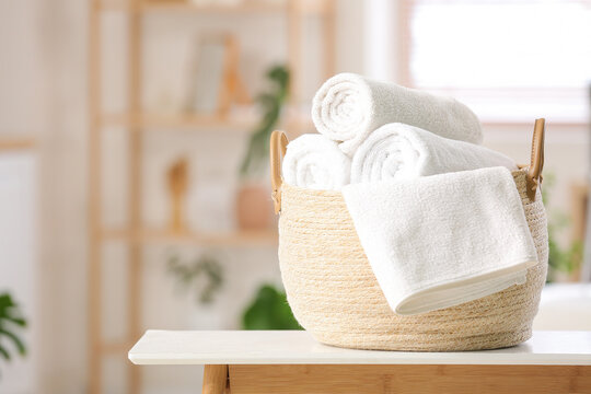Basket with clean soft rolled towels on table in bathroom