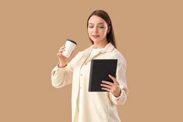Naklejka premium Beautiful young woman with modern tablet computer and paper cup of coffee on brown background