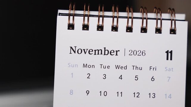 Close-up of a desk calendar on a laptop keyboard as a finger points to a date in November 2026. Static camera focuses on precise date indication and structured monthly planning in a modern workspace.