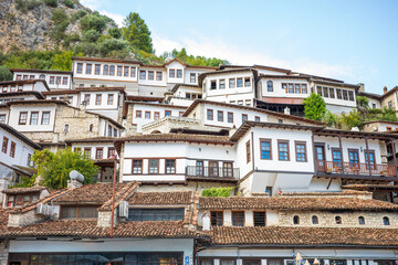 Obraz premium Rows of beautifully preserved white stone houses with wooden balconies and red tiled roofs rise along a lush green hillside, creating a stunning historic old town panorama