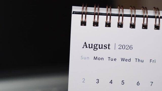Close-up of a desk calendar on a laptop keyboard as a human finger points to a specific date in August 2026. Static camera highlights precise date indication and structured monthly planning in a mode