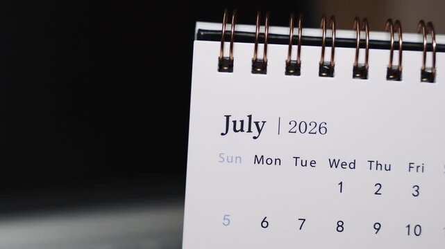 Close-up of a desk calendar on a laptop keyboard as a human finger points to a specific date in July 2026. Camera remains static, emphasizing clear date indication and focused monthly planning concep