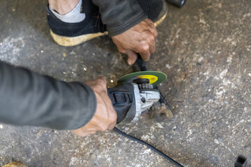 Close up of man hands with intense concentration cutting metal. skilled worker operates an angle grinder, power tool for an industrial job in workshop on concrete floor