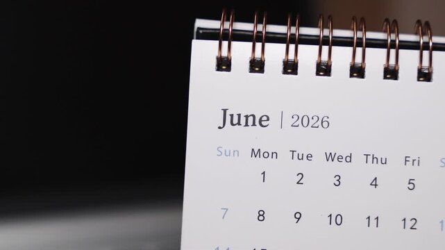 Close-up of a desk calendar placed on a laptop keyboard as a human finger points to a specific date in June 2026. Static camera highlights precise date selection and structured monthly planning conce