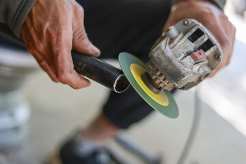 Focused worker man using an angle grinder tool to grind metal pipe. craftsman at work in workshop...