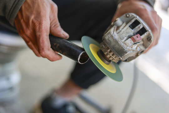Focused worker man using an angle grinder tool to grind metal pipe. craftsman at work in workshop showing skill, industry, and precision with power tool