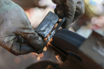 Intense close up of worker grinding metal with bench grinder, creating shower of hot sparks. Wearing protective gloves, craftsman carefully shapes piece of steel with focus