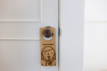 Wooden do not disturb sign with cartoon for quiet hangs on hotel room door handle. This simple hanger requests privacy for silent and peaceful rest inside