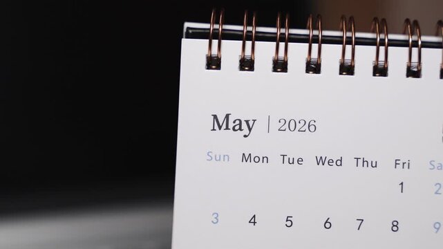 Close-up of a desk calendar on a laptop keyboard as a human finger points to a specific date in May 2026. Camera remains static, presenting clear date indication and calm monthly planning concept ind