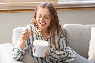 Young woman with ice cream bucket sitting on sofa at home © Pixel-Shot