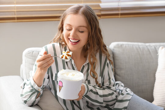 Young woman with ice cream bucket sitting on sofa at home