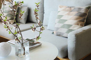 Cozy sofa, coffee table and vase with blooming branches in living room