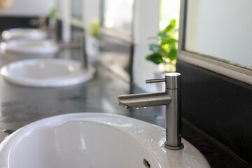 Clean modern bathroom interior design with row of white ceramic sinks and steel faucet. feeling of freshness and hygiene in public washroom or luxury spa