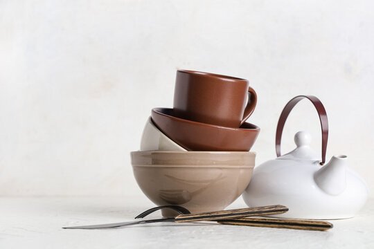 Stack of brown clean tableware and teapot on white background