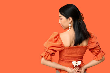 Young Asian woman with white gerbera flower on orange background