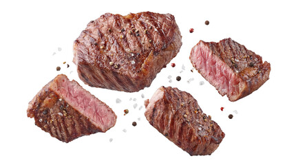 four delicious grilled steak cuts seasoned with salt and pepper, displayed with whole peppercorns and coarse sea salt on black.