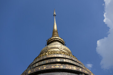 Naklejka premium Majestic gold stupa of an ancient Thai temple under peaceful blue sky. Serene spiritual architecture representing religion, history, landmark, and tranquility in Asia