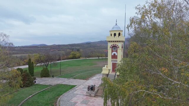 A cinematic reveal of the Čegar Memorial Monument in Ni&scaron; as it appears behind surrounding trees, highlighting its historical significance and the calm natural setting of the memorial park.