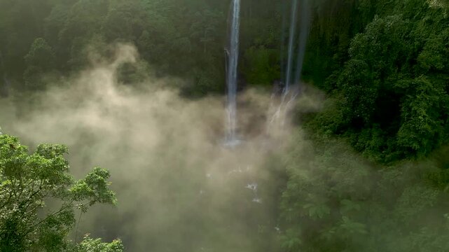 Drone aerial view of Sekumpul Waterfall in Bali, Indonesia, at sunrise with misty atmosphere, cascading water and lush tropical rainforest.