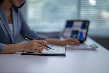 Businesswoman analyzing financial charts and data on laptop and documents at office desk