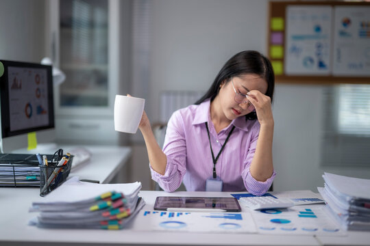 Young office worker drinking coffee while working with a computer and having a bad headache