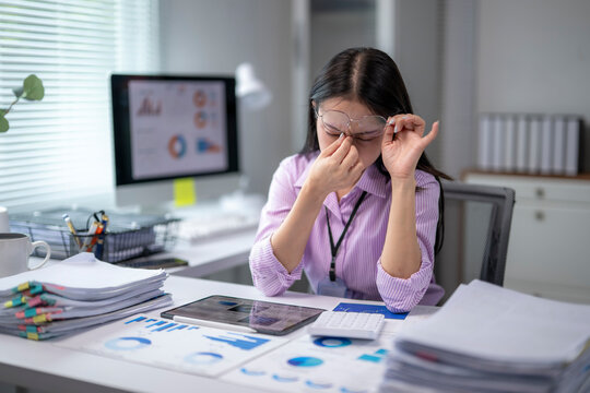 Tired asian businesswoman rubbing her eyes at office desk after long computer work