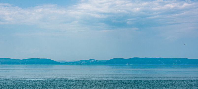 Wide view of the Saint Lawrence River near Gasp&eacute;sie, Quebec, with calm blue water, distant mountains and dramatic clouds, creating a serene coastal landscape with copy space.