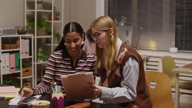 Young zoomer generation coworkers discussing ideas and working together in creative office, using tablet and desk supplies, representing teamwork, collaboration and modern work culture