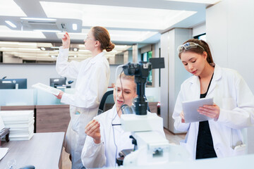 Obraz premium Asian female scientist using tablet to discuss histology results with colleague at microscope. Team collaborating on digital pathology analysis in modern lab.