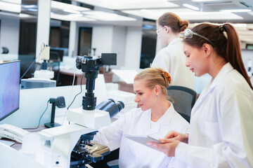 Obraz premium Asian female scientist using tablet to discuss histology results with colleague at microscope. Team collaborating on digital pathology analysis in modern lab.