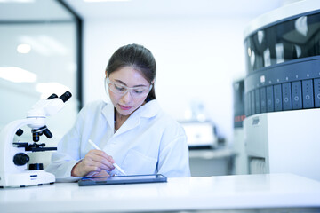 Focused female scientist using a microscope and digital tablet to analyze research data in a modern sterile laboratory. Professional medical researcher working on disease diagnosis projects.