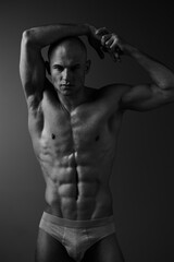 Naklejka premium Black and white image of a muscular man posing confidently, showcasing his toned physique and strength. Strong lighting emphasizes the contours and shadows on his body.