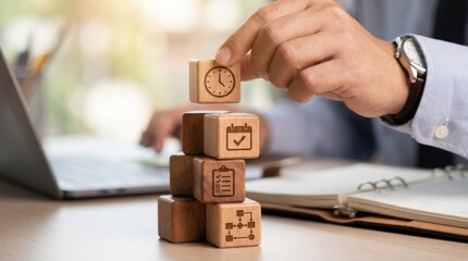 Professional hand wearing business shirt and leather watch stacks natural wood blocks engraved with clock and planning icons on a desk.