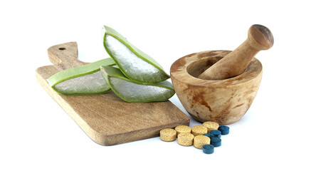 Aloe vera slices and pills next to a wooden mortar and pestle on a cutting board
