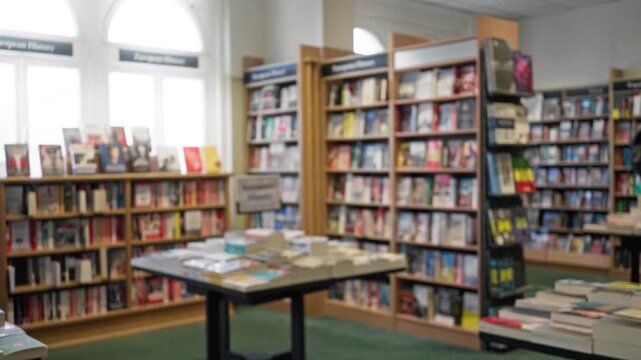 Blurry indoor library scene with defocused bookshelves filled with colorful textbooks and tables under bright lighting creates a calm scholarly atmosphere.