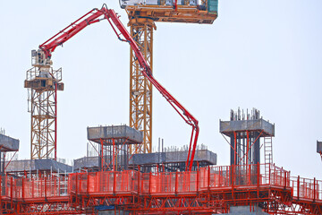 Construction site with red concrete pump and crane is actively working on building structure. scene includes scaffolding and metal reinforcements under clear sky