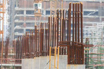 Steel reinforcement bars protrude from concrete columns at construction site, showcasing early stages of building development. background features cranes and scaffolding