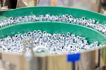 Hex Nuts on Vibratory Feeder Bowl in Factory. Shiny hexagonal metal nuts being aligned and sorted on a green vibratory feeder in an automated industrial environment. Selected focus
