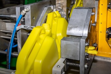 Industrial blow molding machine producing yellow plastic canister. Industrial plastic injection molding process in a factory environment. Selected focus