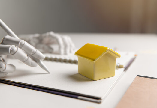 Robotic Hand Writing Notes Near Small House Model for AI Real Estate Concept