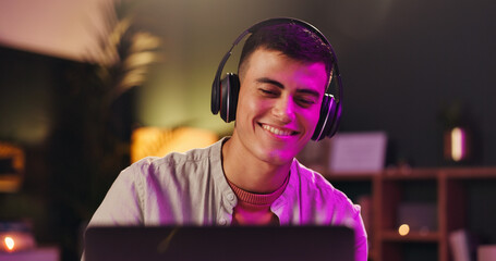 Laptop, musician and smile with headphones for production, audio or listen to music track. Computer, man and streaming song with tech for content creator, subscription and neon light at night in home © WesJVR/peopleimages.com