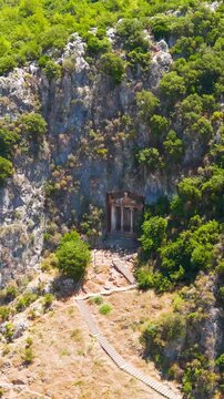 Vertical video. Fethiye, Turkey. Archaeological exploration of the Lycian rock tombs and the famous Tomb of Amyntas from 350 BC in the cliffs, drone view.. Aerial View, Departure of the camera. Rich 