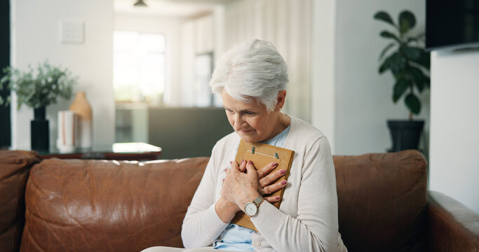 Photograph, reflection and sad with old woman on sofa in living room of home for grief, loss or pain. Picture frame, remember and senior person with depression in apartment for memories or nostalgia