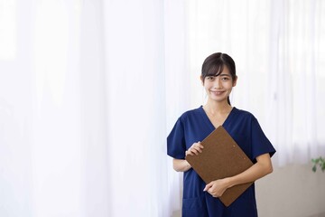 Smiling Young Female Healthcare Worker in Navy Scrubs Holding Clipboard
