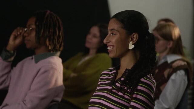 Diverse group of young people sitting in audience during creative public event, listening attentively and smiling while watching presentation in professional setting
