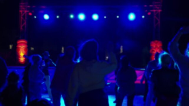 Blurred silhouettes of people dancing at a disco in a nightclub, bar or restaurant. People relaxing and having fun at a party. The bright light of the floodlights.