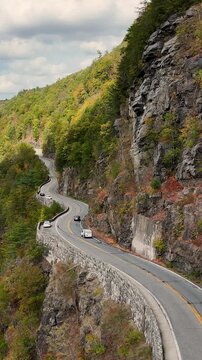 Aerial footage of Hawks Nest Lookout along NY-97 in the Catskills, showing a winding cliffside highway above the Delaware River surrounded by fall forest and mountain terrain.