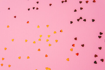 Shining gold heart confetti scattered brightly on a soft pink surface for Valentine's Day