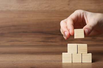 Woman building pyramid of cubes on wooden background, closeup with space for text. Idea concept © Aashir